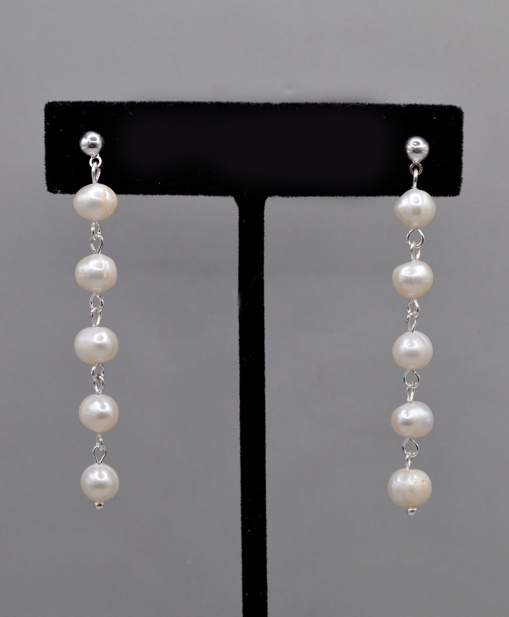 Long pearl strand earrings featuring graduated freshwater-style pearls linked in a graceful linear drop, product view at…