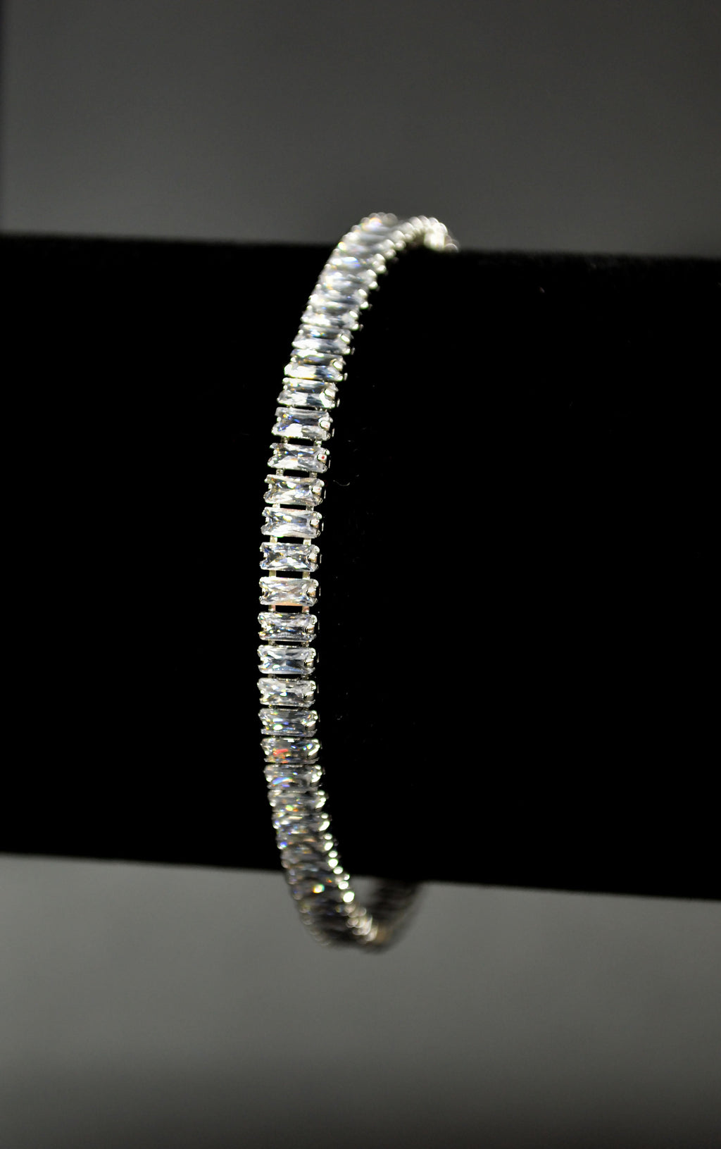 Baguette crystal tennis bracelet featuring continuous line of rectangular stones in a sleek setting, detail view at…