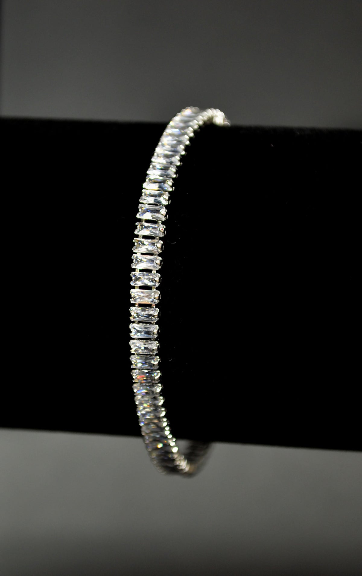 Baguette crystal tennis bracelet featuring continuous line of rectangular stones in a sleek setting, detail view at…