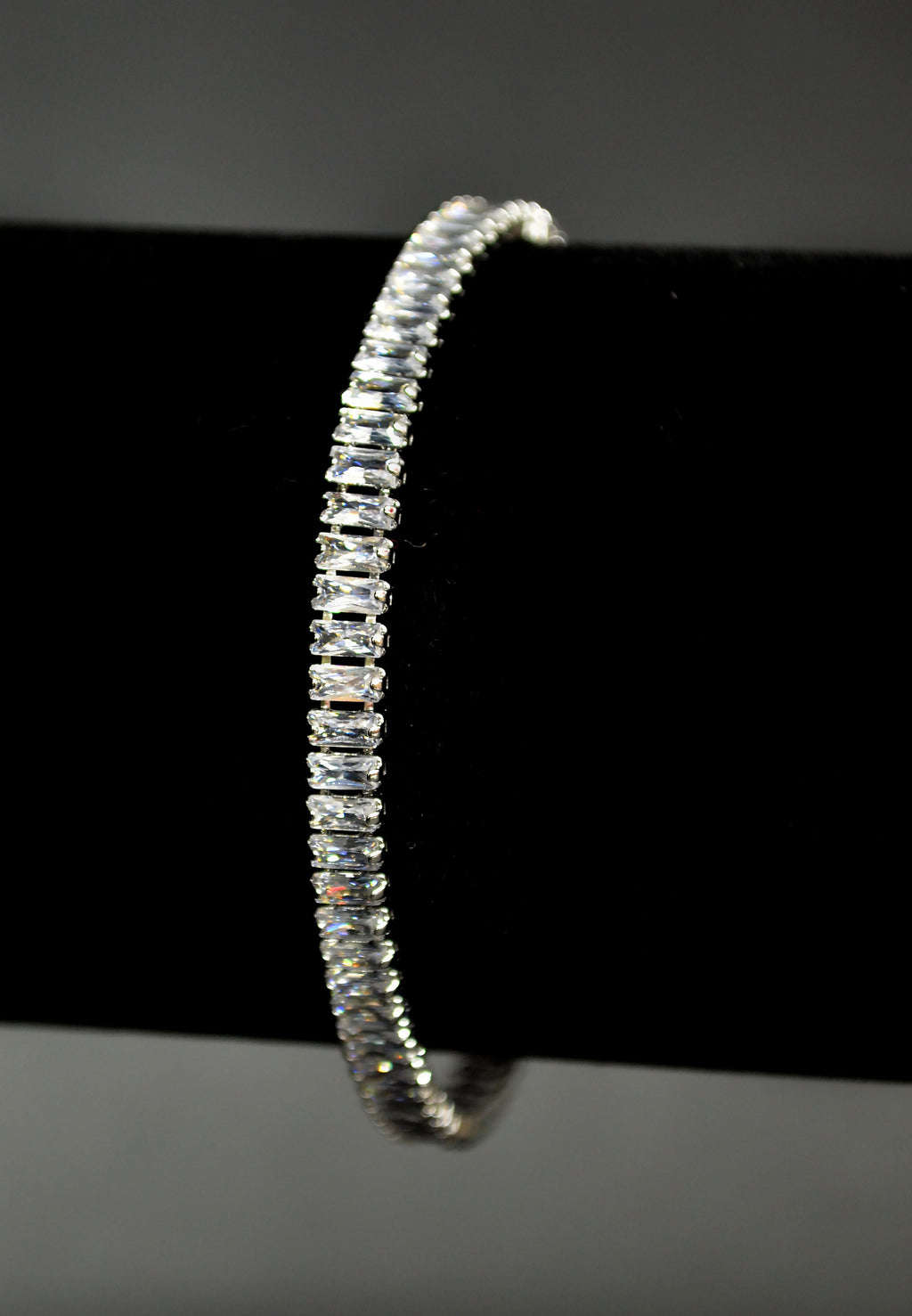 Baguette crystal tennis bracelet featuring continuous line of rectangular stones in a sleek setting, product view at…