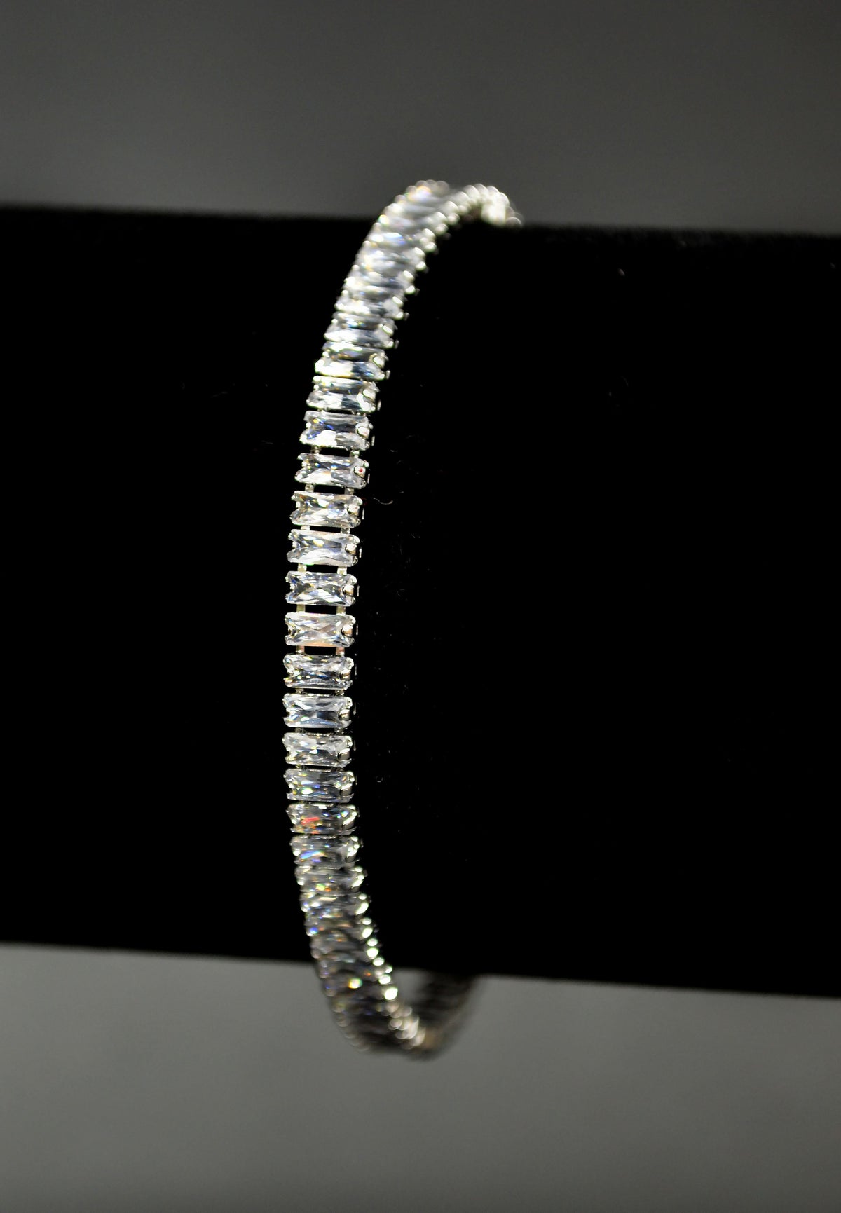 Baguette crystal tennis bracelet featuring continuous line of rectangular stones in a sleek setting, product view at…