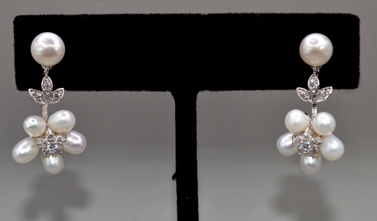 Pearl flower drop earrings featuring pearl stud with a delicate cluster of pearls and crystal leaves, product view at…