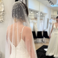 Dramatic pearl wedding veil featuring oversized and scattered pearls cascading from crown to train. Modern bridal accessory paired with a sleek satin wedding dress at Rebecca's Wedding Boutique.